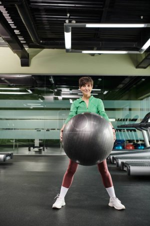 mujer feliz haciendo ejercicio con la pelota de fitness en el gimnasio, senior activo, fitness y deporte, desgaste activo