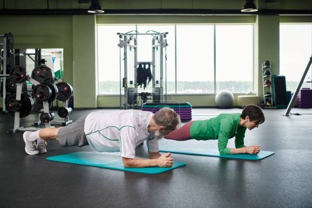 anciano y mujer haciendo tablón en colchonetas de fitness, personas mayores activas haciendo ejercicio en el gimnasio, vida sana