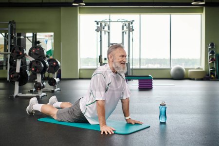 homme âgé heureux avec barbe étirant en arrière sur tapis de fitness, senior actif, vibrant et en bonne santé