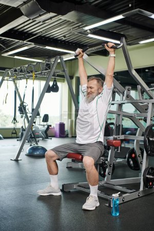 strong and elderly man with beard working out on exercise machine, athletic and healthy, full length