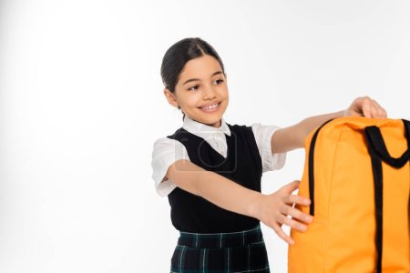 positive schoolgirl taking backpack isolated on white, back to school concept, girl in uniform, joy