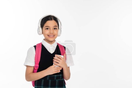 digitales Zeitalter, fröhliches Schulmädchen mit drahtlosen Kopfhörern, Smartphone isoliert auf weiß, Student