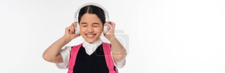 fröhliches Schulmädchen mit drahtlosen Kopfhörern, das isoliert auf weißen, geschlossenen Augen Musik hört, Banner