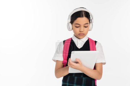 écolière concentrée dans les écouteurs sans fil en utilisant une tablette numérique isolée sur blanc, âge numérique