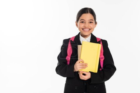 happy schoolgirl looking at camera and holding notebooks isolated on white, student, back to school