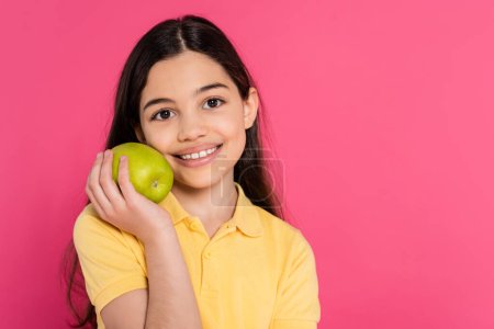 portrait de fille brune heureuse tenant pomme verte et fraîche isolée sur fond rose, vibrant