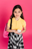 schoolgirl looking at camera and holding smartphone isolated on pink, backpack, vibrant and bright t-shirt #670362320