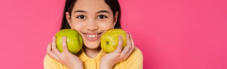 happy girl with brunette hair holding green apples on pink background, portrait, happiness, banner