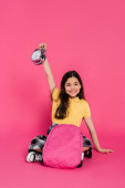 positive and brunette schoolgirl sitting with backpack, holding vintage alarm clock on pink Sweatshirt #670362886
