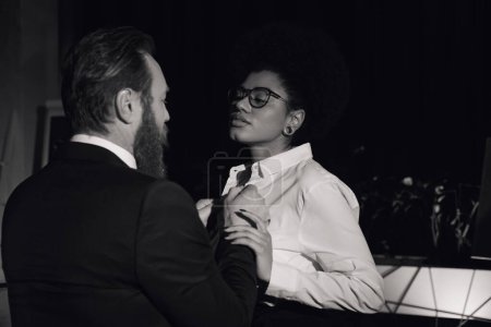 black and white image of bearded businessman undressing african american woman at high in office