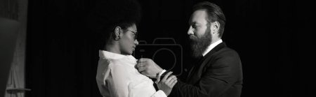 Photo for Monochrome photo of bearded man undressing young african american businesswoman in office, banner - Royalty Free Image