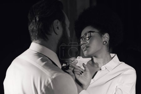 Foto de Foto monocromática de mujer afroamericana en anteojos seduciendo a hombre de negocios barbudo en la oficina - Imagen libre de derechos