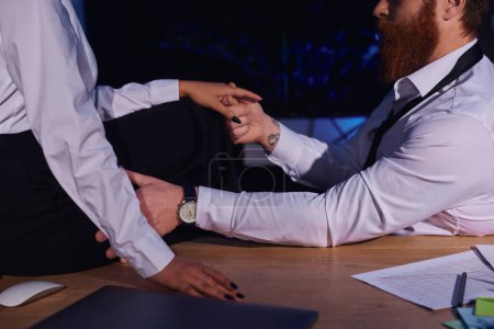 Photo for Bearded tattooed businessman holding hand of african american woman sitting on desk, cropped view - Royalty Free Image