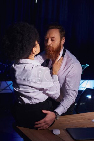 joven mujer afroamericana y hombre de negocios barbudo abrazándose en la noche en la oficina, encuentro romántico
