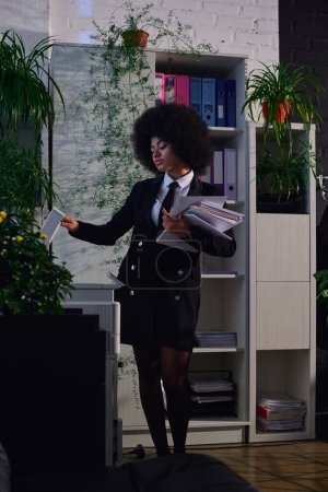 Afroamerikanerin in eleganter formaler Kleidung kopiert Dokumente, während sie nachts im Büro arbeitet