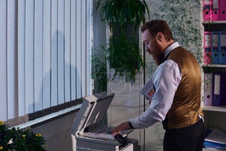 Téléchargez les photos : Vue latérale de l'homme d'affaires barbu élégant en tenue formelle photocopiant des documents au bureau la nuit - en image libre de droit