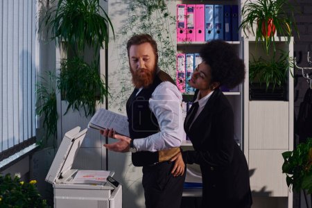 young african american woman seducing bearded businessman standing with documents near copier