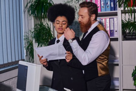 barbudo empresario tocando cara de joven secretario con documento cerca de fotocopiadora en la oficina, el coqueteo