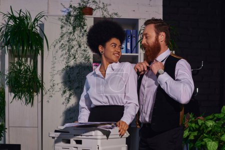 bearded businessman flirting with smiling african american secretary standing near copier in office