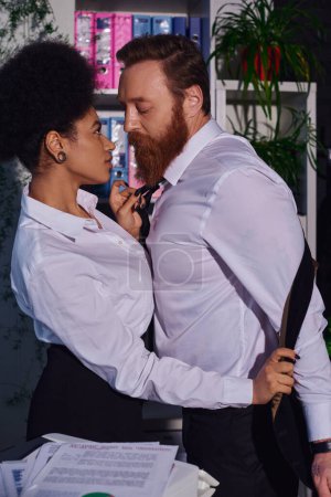 Téléchargez les photos : Tentante femme d'affaires afro-américaine déshabillée collègue barbu au bureau, vue de côté - en image libre de droit
