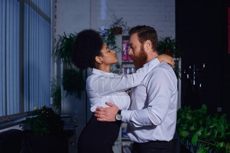 Photo for Side view of charming african american secretary seducing bearded businessman in office at night - Royalty Free Image