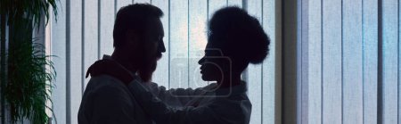 Téléchargez les photos : Silhouette sombre de femme afro-américaine embrassant homme d'affaires barbu la nuit au bureau, bannière - en image libre de droit