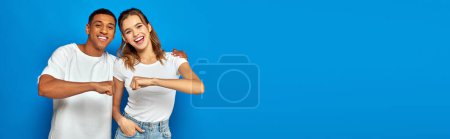 Téléchargez les photos : Bannière, couple interracial poing cognant sur fond bleu, homme afro-américain et femme excitée - en image libre de droit
