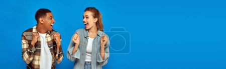 Photo for Happy interracial couple screaming from joy looking at each other on blue backdrop, banner - Royalty Free Image