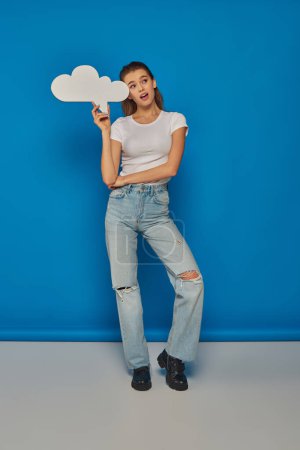 Photo for Pensive young woman with open mouth looking away and holding blank thought bubble on blue background - Royalty Free Image