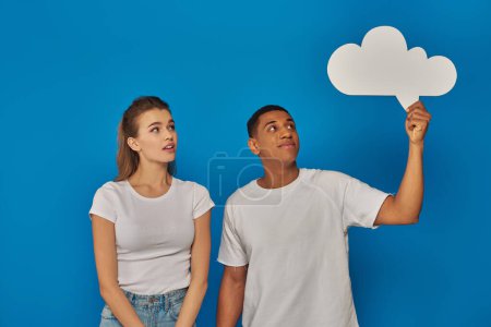 african american man holding blank thought bubble near pretty young woman on blue background