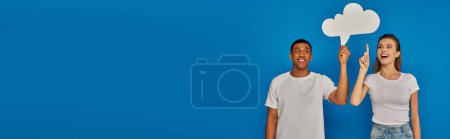 Photo for Multicultural couple smiling and pointing with fingers at thought bubble on blue backdrop, banner - Royalty Free Image