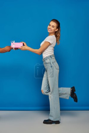 Afrikanisch-amerikanischer Mann beschenkt aufgeregte Frau auf blauem Hintergrund, festliche Anlässe
