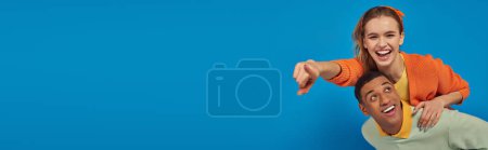 Photo for Banner, joyful african american man piggybacking girlfriend on blue background, pointing at camera - Royalty Free Image