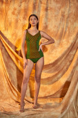 young asian woman posing in green swimwear with hand on hip on beige background with drapery Stickers #672002834