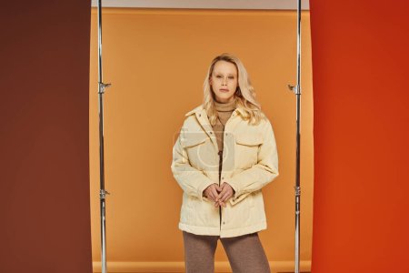 autumn fashion concept, blonde woman in warm jacket posing on orange backdrop, cozy layers