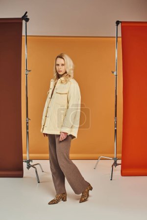 Herbst-Modekonzept, blonde Frau im Herbst-Outfit und Animal-Print-Stiefel posieren auf orangefarbenem Hintergrund