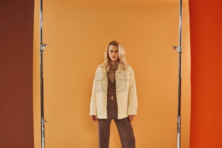 Téléchargez les photos : Attrayant femme en tenue d'automne regardant la caméra et posant sur fond beige, couches confortables - en image libre de droit