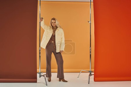 beautiful blonde model in autumn outfit looking at camera and posing on pastel backdrop, outerwear