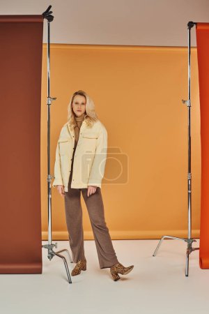 hübsche Frau in Oberbekleidung und Stiefeln, die in die Kamera schaut, während sie vor pastellfarbenem Hintergrund posiert, Animal Print