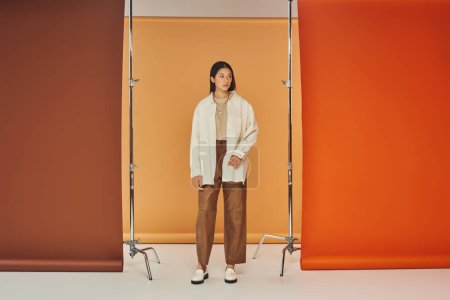 hübsche Asiatin posiert im Herbst-Outfit, Lederhose und Oberbekleidung, buntem Hintergrund