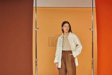 jolie femme asiatique en tenue d'automne posant avec la main dans la poche, pantalon en cuir et vêtements de dessus
