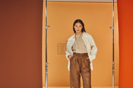 Téléchargez les photos : Jeune femme asiatique en tenue d'automne posant avec les mains dans les poches, pantalon en cuir et vêtements de dessus - en image libre de droit