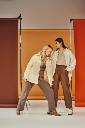 fall fashion, young interracial women in autumn clothes posing on pastel multicolored backdrop