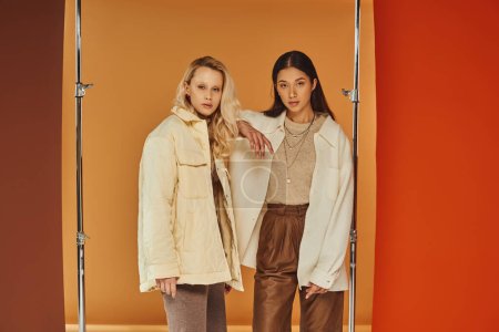 Herbstmode, junge interrassische Models in Herbstkleidung posieren vor pastellfarbener Kulisse