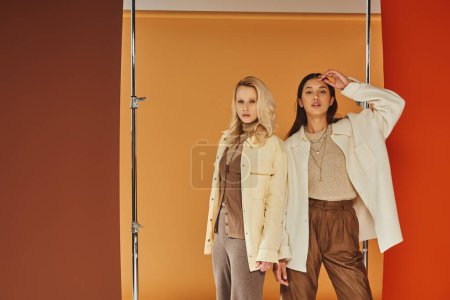Photo for Fall fashion, pretty interracial models in autumn attire posing on colorful pastel backdrop - Royalty Free Image
