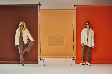 Herbstmode, stylische multikulturelle Models in Sonnenbrille und Oberbekleidung posieren vor buntem Hintergrund