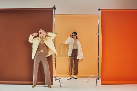 Herbstsaison, multiethnische Models in Sonnenbrille und Herbst-Oberbekleidung posieren vor buntem Hintergrund