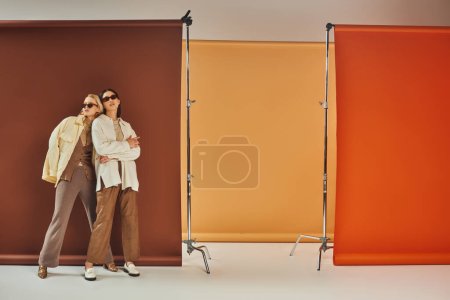Temporada otoñal, modelos multiétnicos en gafas de sol y ropa de abrigo de otoño posando sobre un colorido telón de fondo