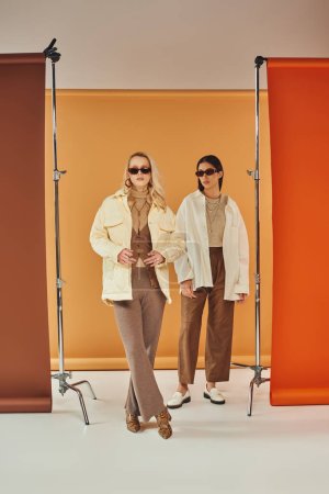 Foto de Modelos interracial en gafas de sol y ropa de abrigo de otoño posando en estudio, colores de otoño, telón de fondo dúo - Imagen libre de derechos