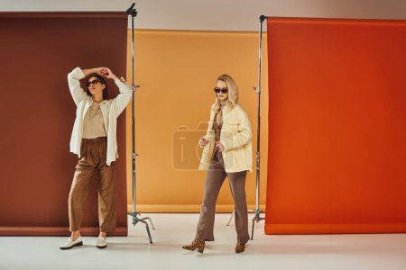 diverse cultures models in autumn outerwear and sunglasses posing on colorful backdrop, fall fashion